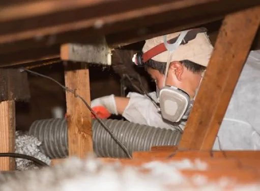 Technician in protective gear working on attic insulation